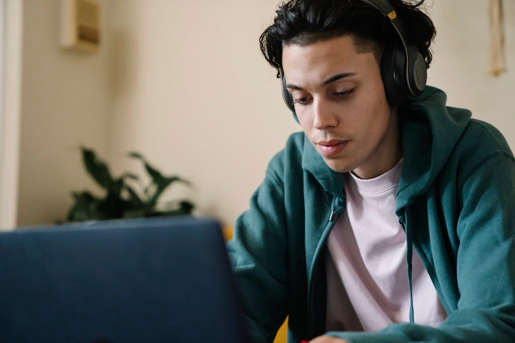 Focused young man studying indoors with headphones and laptop, perfect for education and technology content.